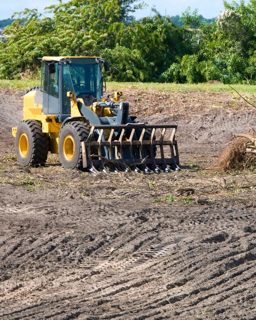 Loader with a root rake parked beside a brush pile on a freshly cleared lot