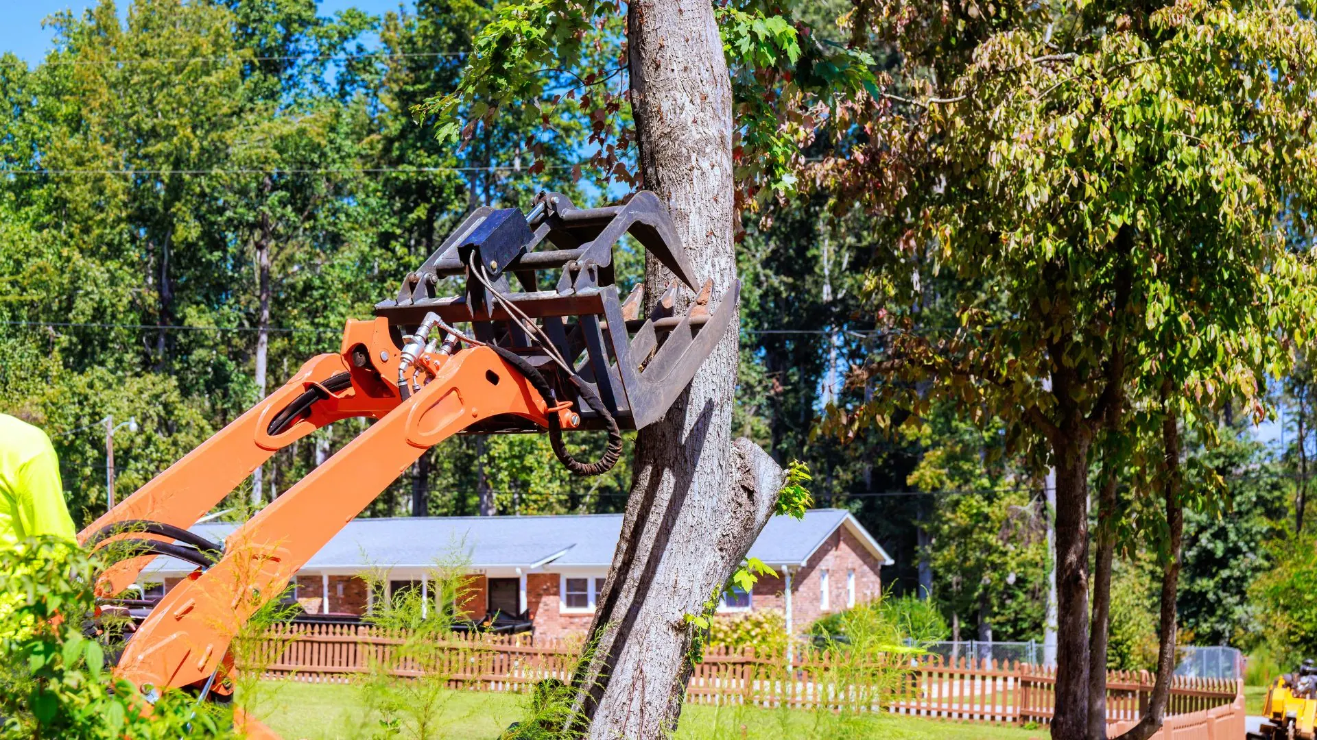 Skid steer grapple carrying a trunk past a ranch house in Belgium